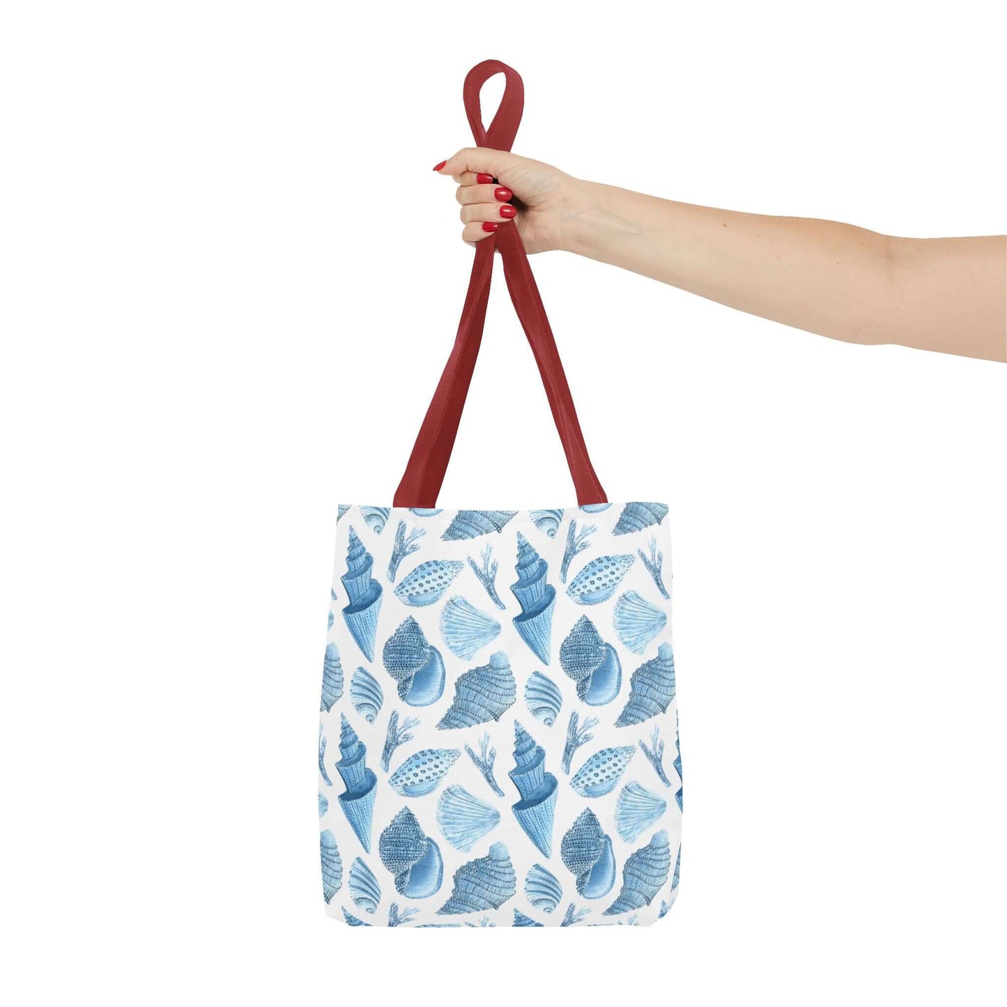 Beachy tote bag with ocean seashells print, held by a hand with red straps, perfect for eco-friendly outings.