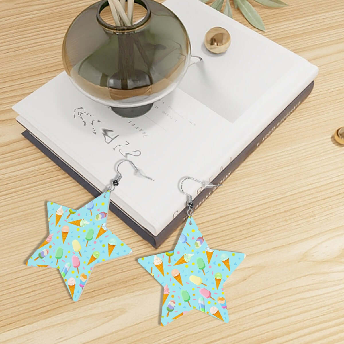 Mint leather star earrings with ice cream pattern, styled on a wooden surface with books and a vase.