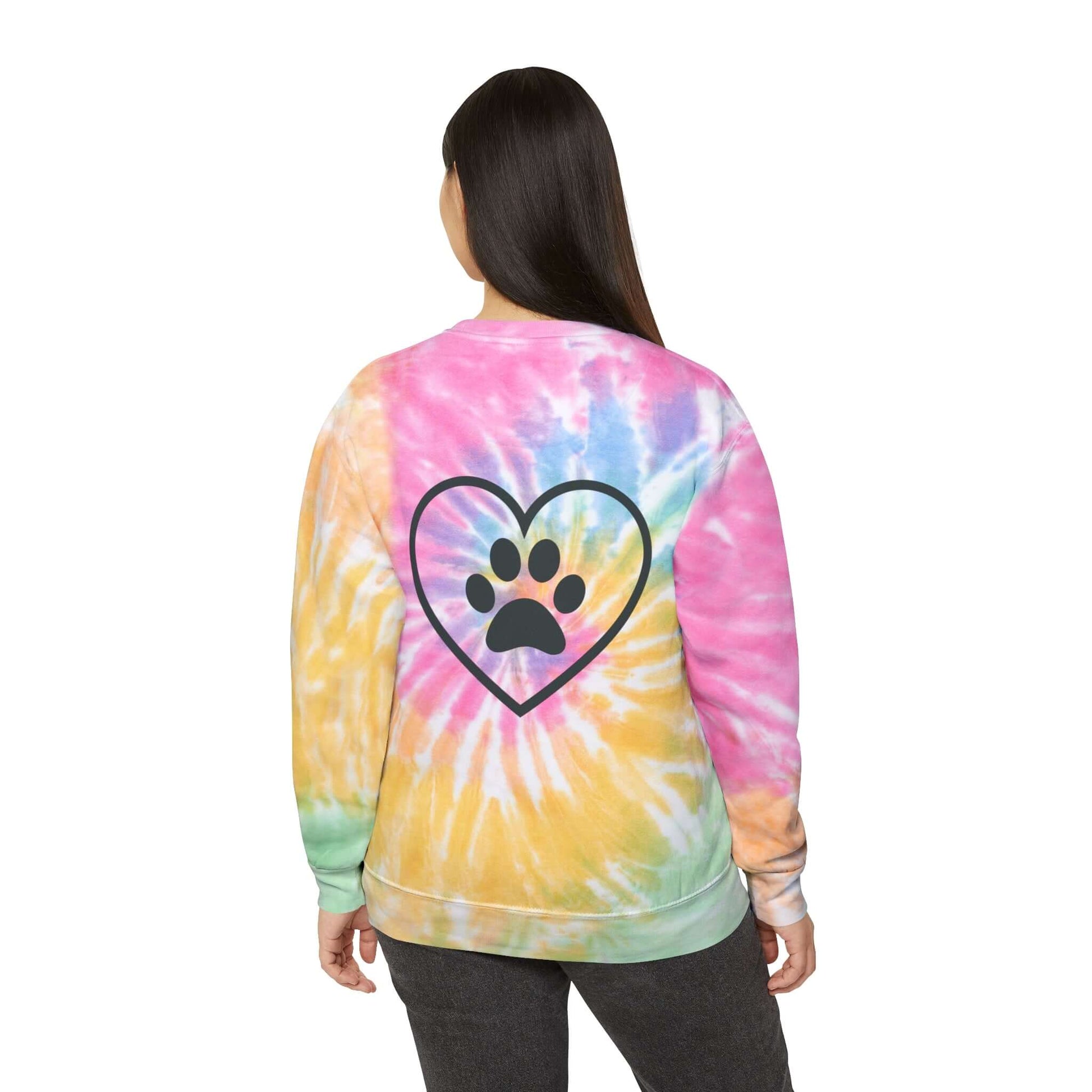 Young Woman wearing a rainbow (Eternity) tie dyed sweatshirt showing the back design featuring an outlined heart with a paw print in the center of it. 