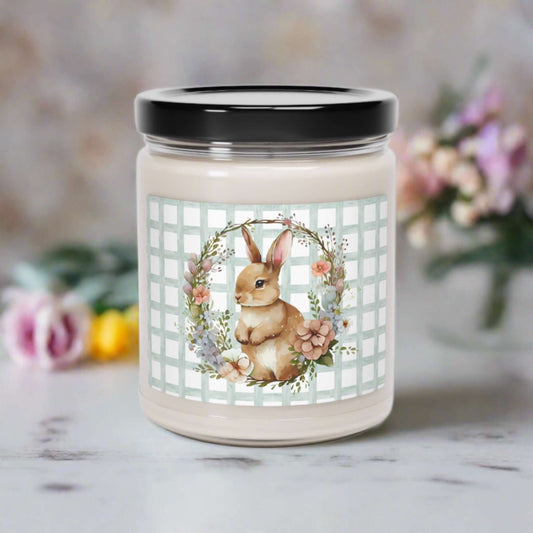 closed glass candle jar with spring themed design featuring a rabbit with a floral wreath on a counter top with flowers behind it