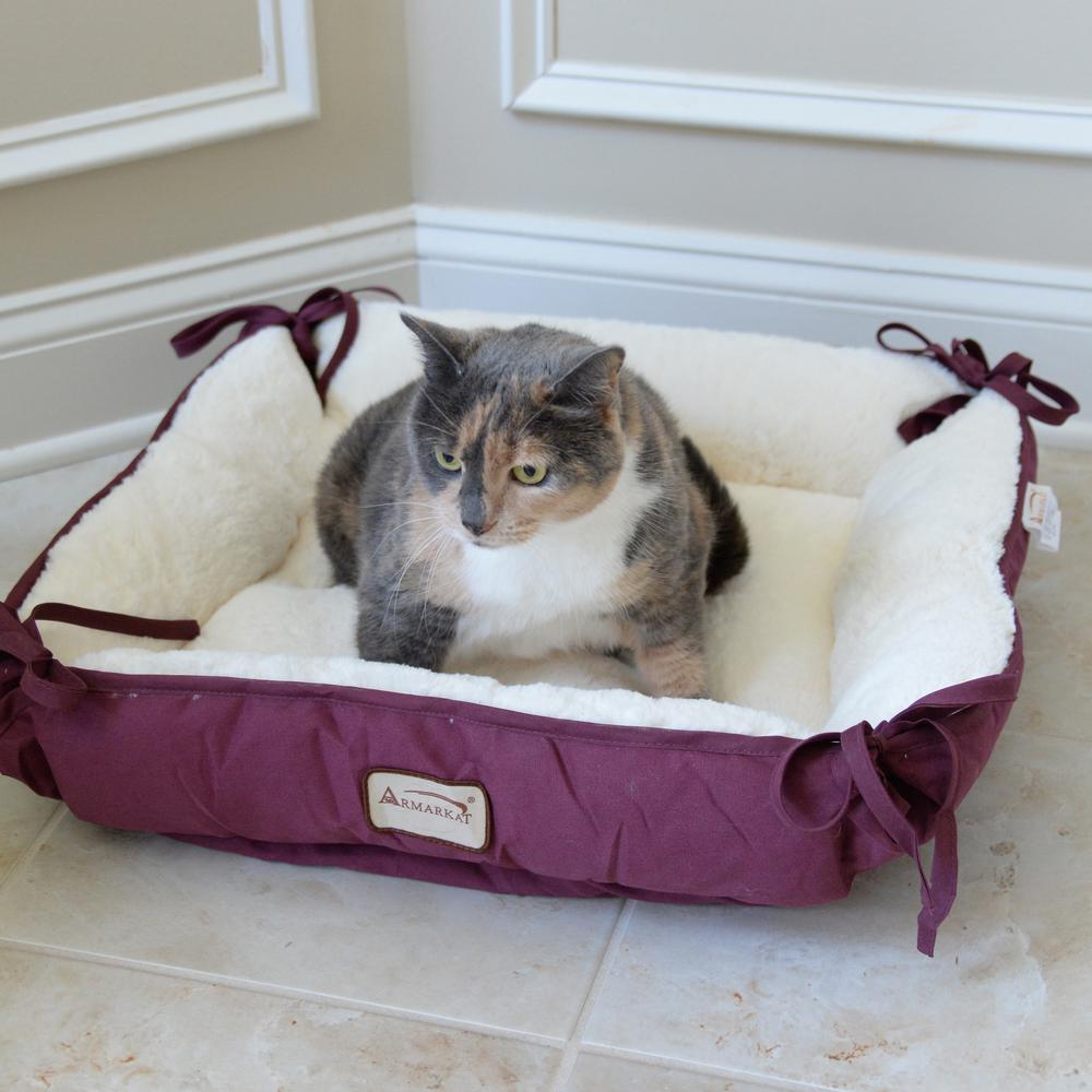 grey calico cat sitting on plush burgundy cat bed 