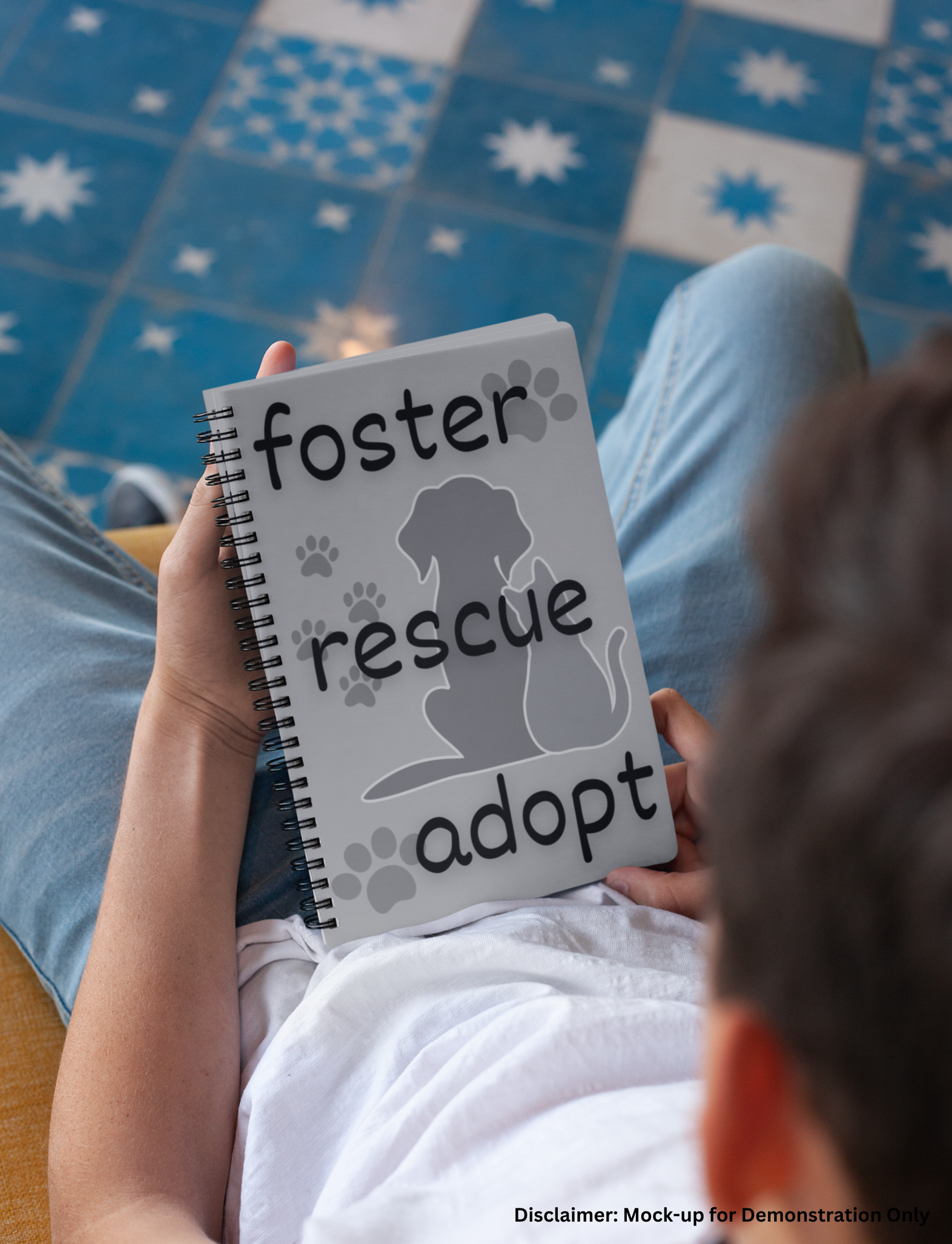 Young Man sitting on a couch holding grey spiral notebook with dog and cat image and the words foster, rescue, adopt on the front