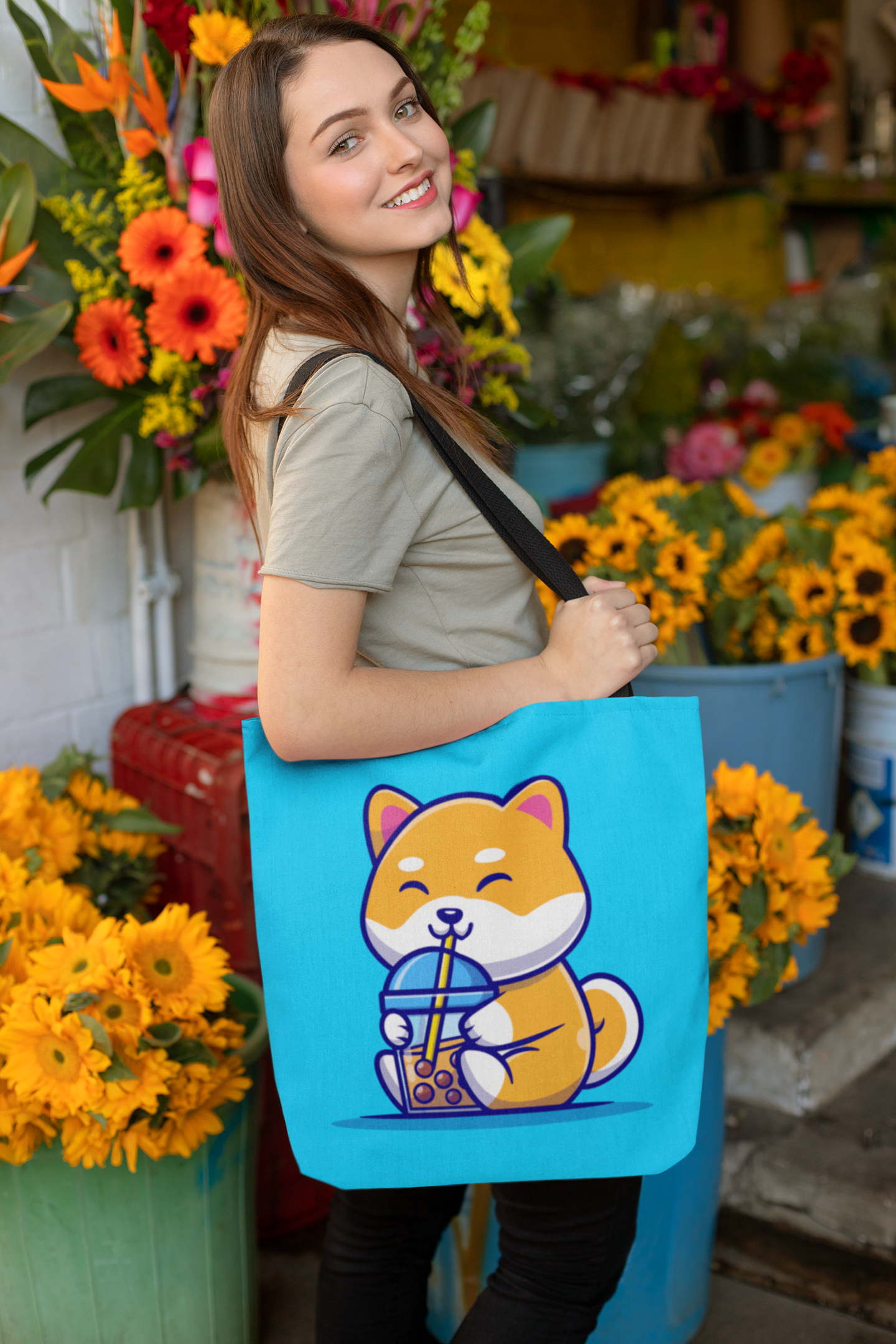 Woman with medium length brown hair standing at the entrance of a flower shop with large turquoise tote bag with a cute shiba inu cartoon drinking boba