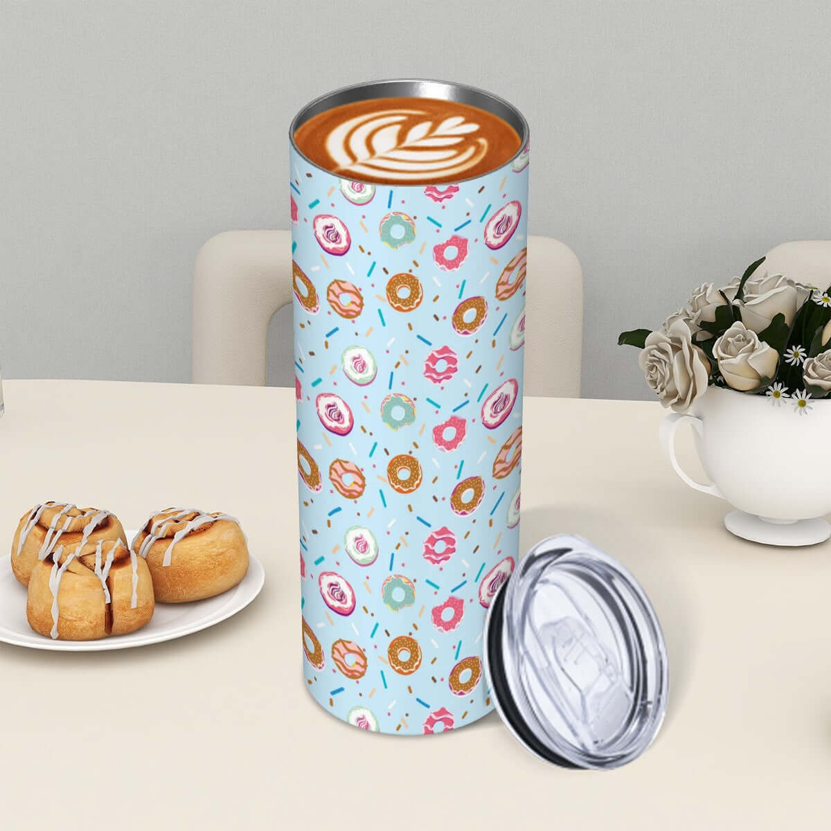 Powder blue stainless steel tumbler with donut designs, coffee latte art, and a plate of donuts on a table.